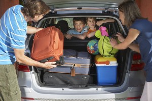 Two young sons watching parents load luggage in car trunk