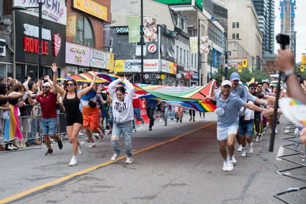 People at the Toronto Pride Parade holding up a large Pride flag.