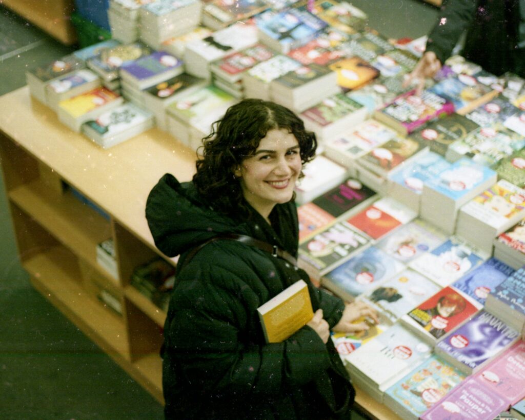 Person smiling at a camera in a bookstore.